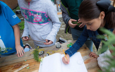Student writing in notebook outside with other students