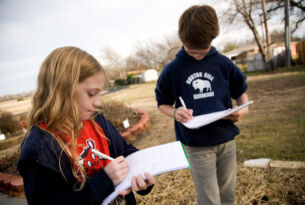 Two students in a garden writing on their notebooks