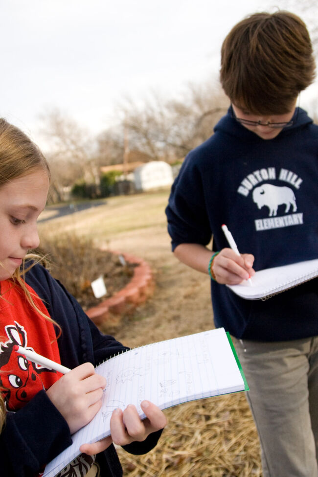 Two students in a garden writing on their notebooks